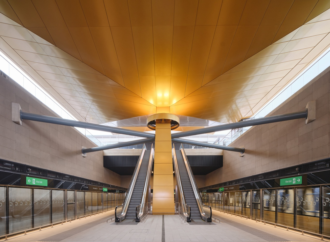 Lower level platform with escalators flanking a yellow-clad column beneath the angled timber ceiling
