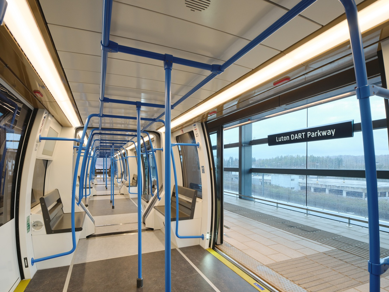 Train carriage interior with blue handrails and platform visible through doors on overcast day