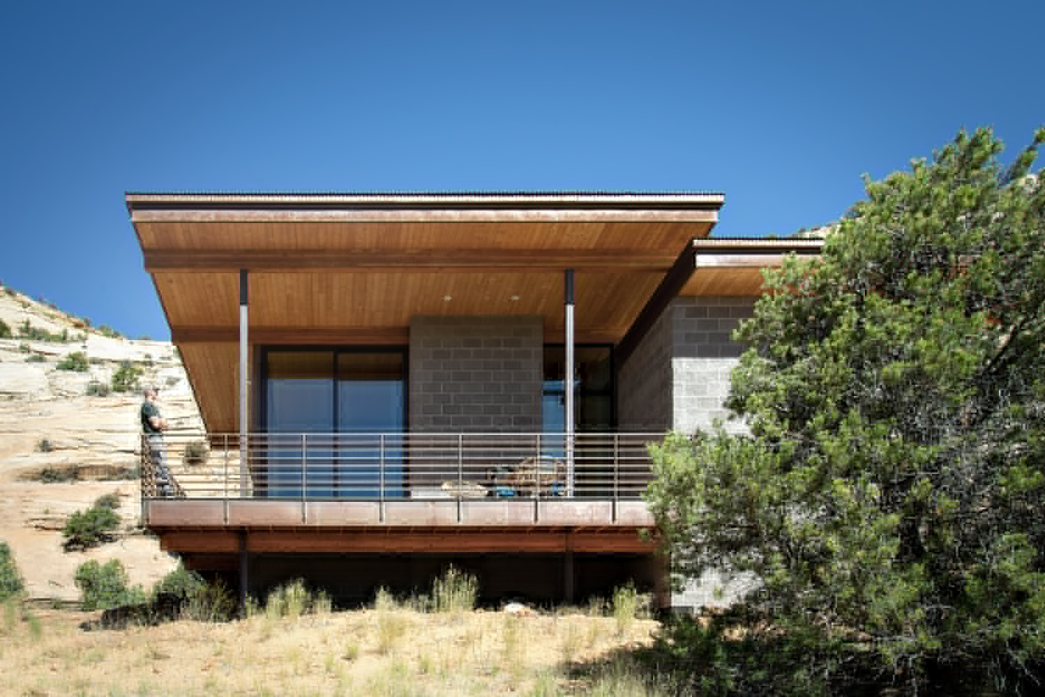 Elevated timber and concrete block residence with horizontal railing deck overlooking a sloping desert hillside