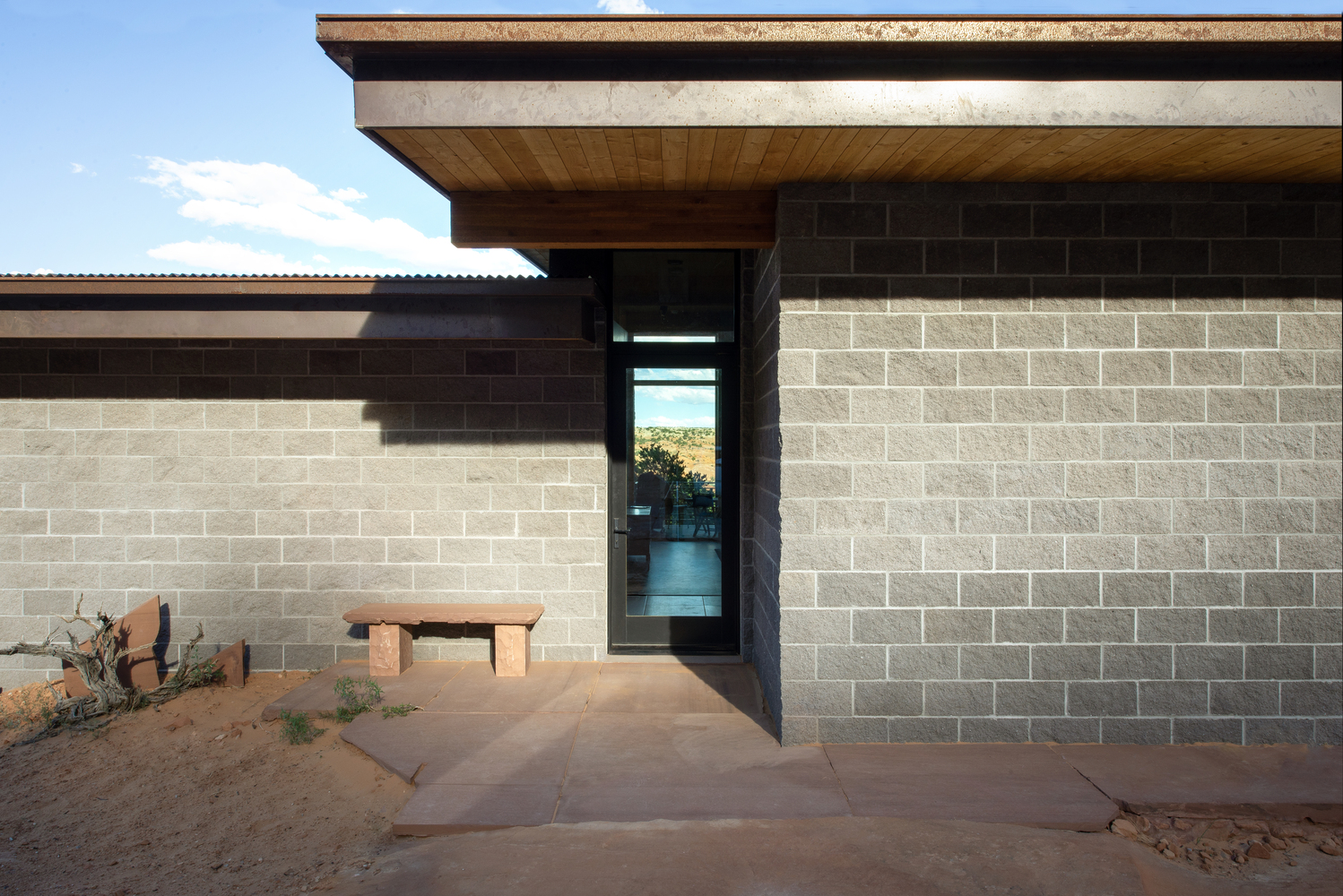Entry facade with two-tone concrete block walls and narrow glazed slot opening beside timber soffit overhang