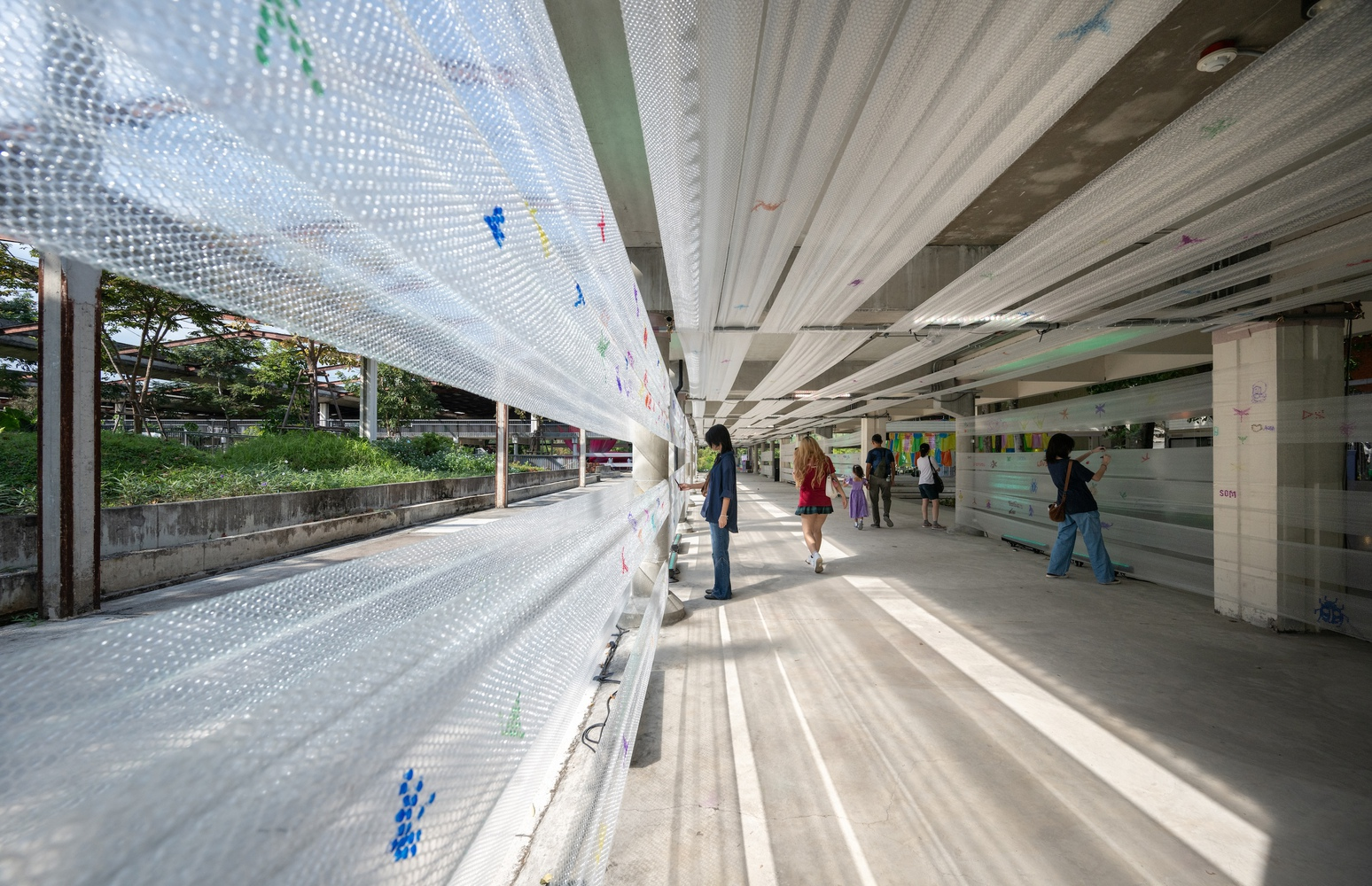 Perforated translucent panels filtering daylight along the open corridor with pedestrians walking through dappled shadows