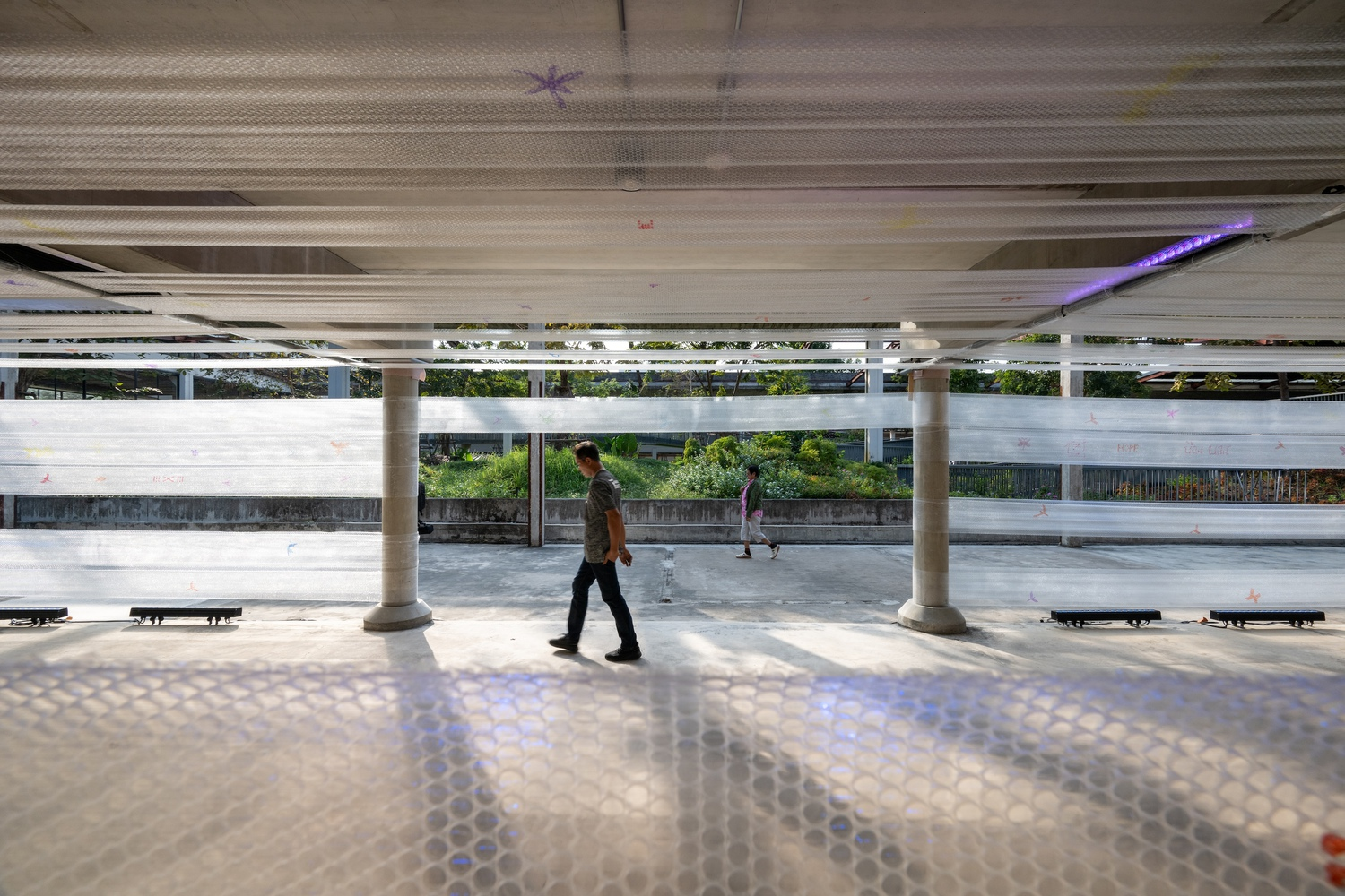 Patterned floor reflecting light from the perforated ceiling as a pedestrian crosses the open plaza