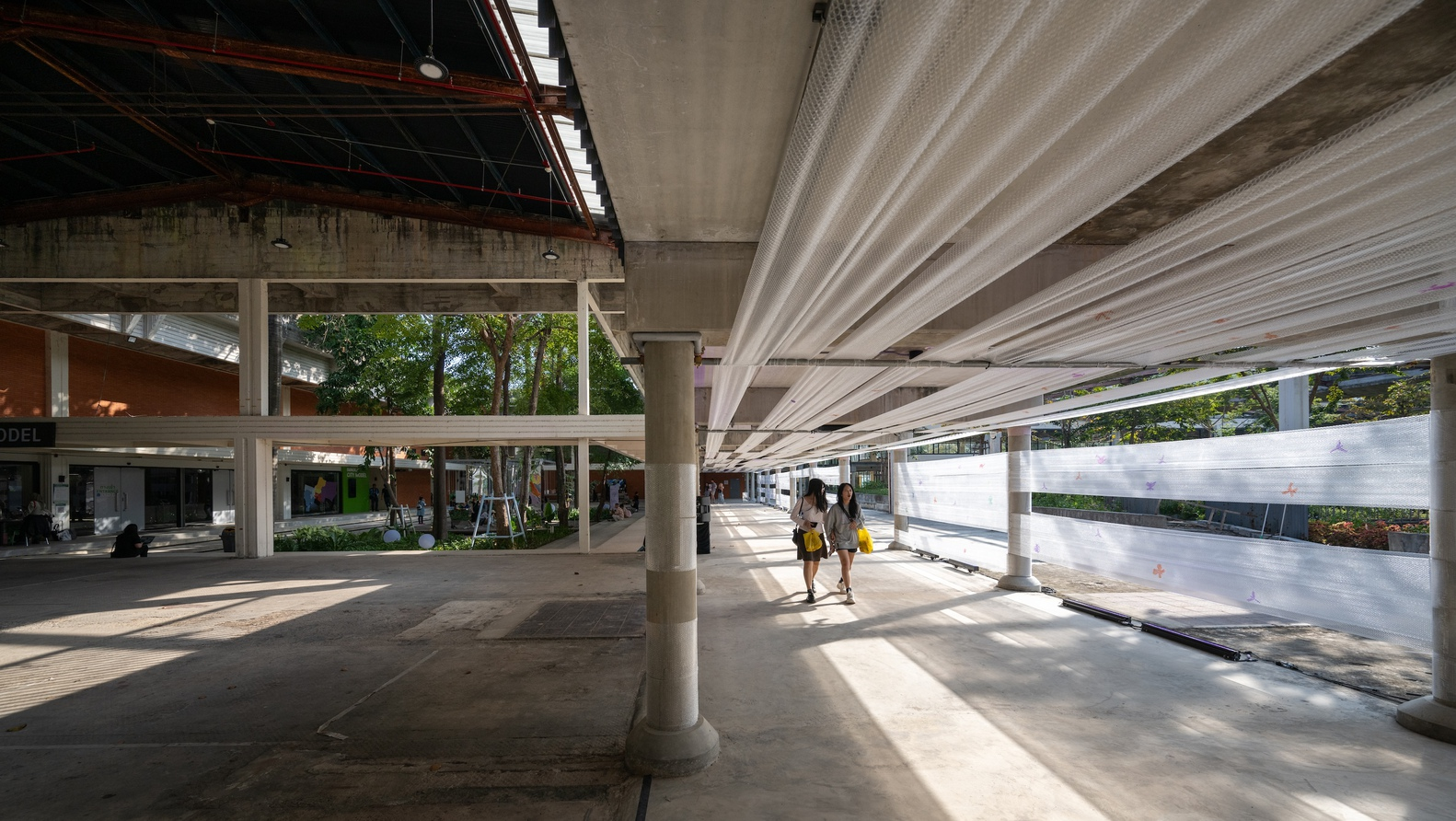 View along the concrete floor with cylindrical columns and fabric screens filtering afternoon sunlight