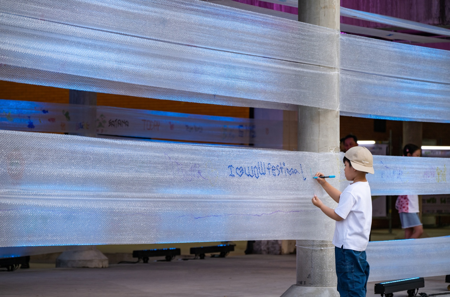 Child writing on translucent horizontal mesh screening wrapping a concrete column