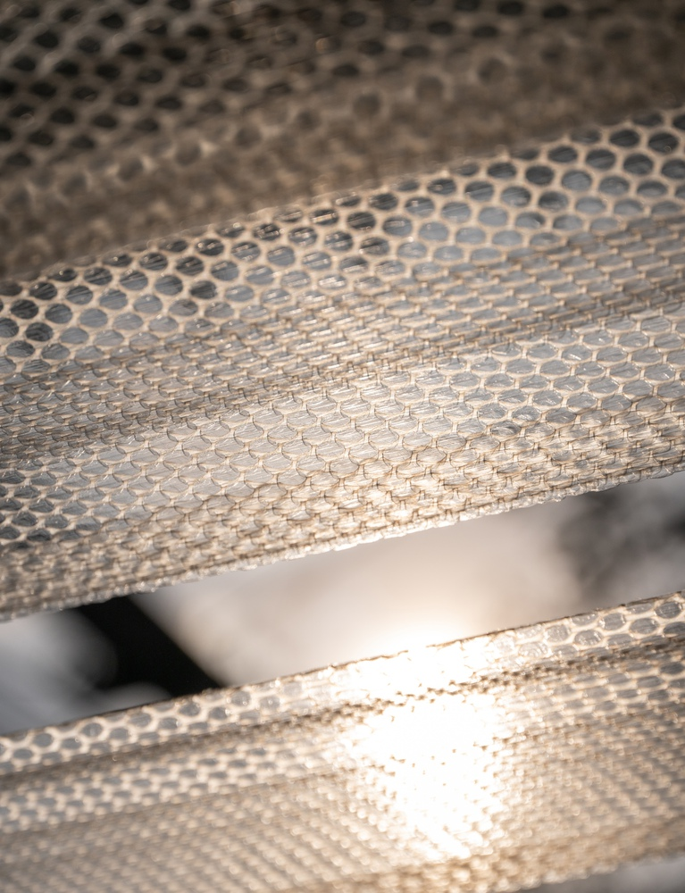 Close-up of layered perforated metal panels with dappled sunlight creating shadow patterns
