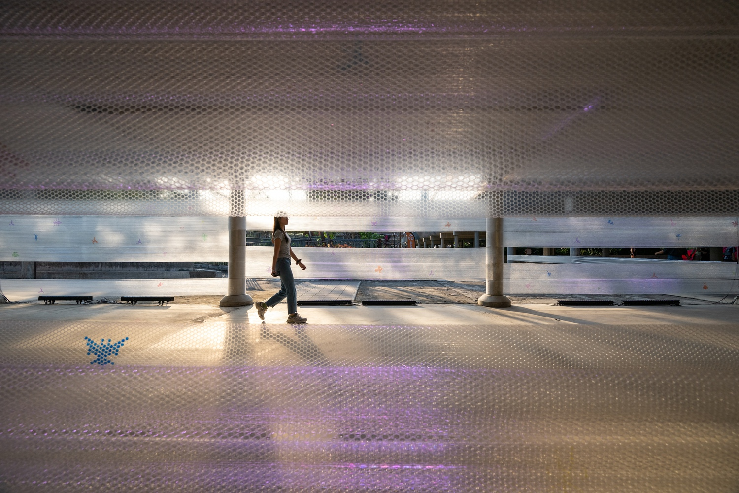 Interior platform with perforated metal ceiling and a lone figure walking past colored floor projections
