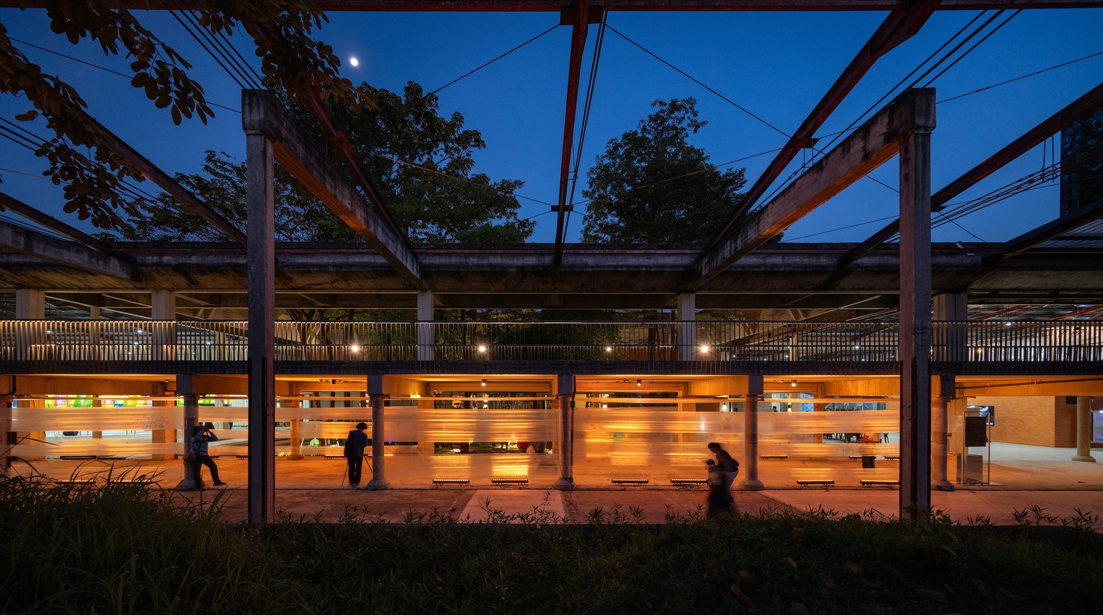 Open-air platform with steel frame structure and timber slat walls glowing at blue hour