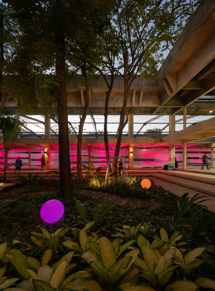 Planted courtyard with illuminated spheres and trees beneath elevated platform structure at twilight