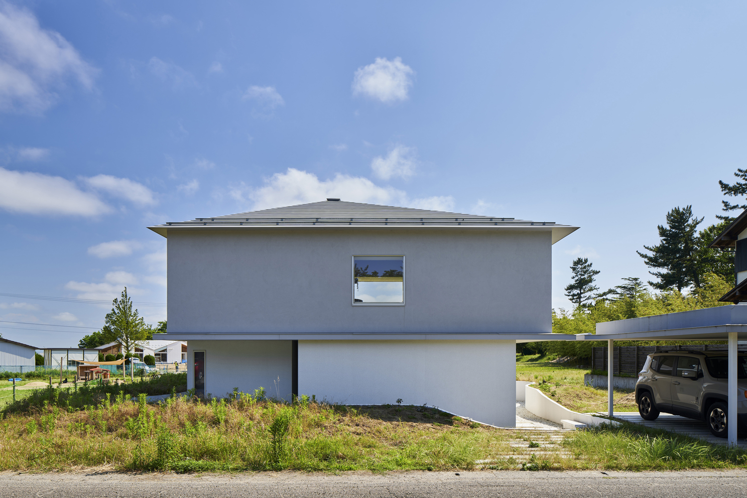 Street view of the white rendered facade with shallow hipped roof under blue sky
