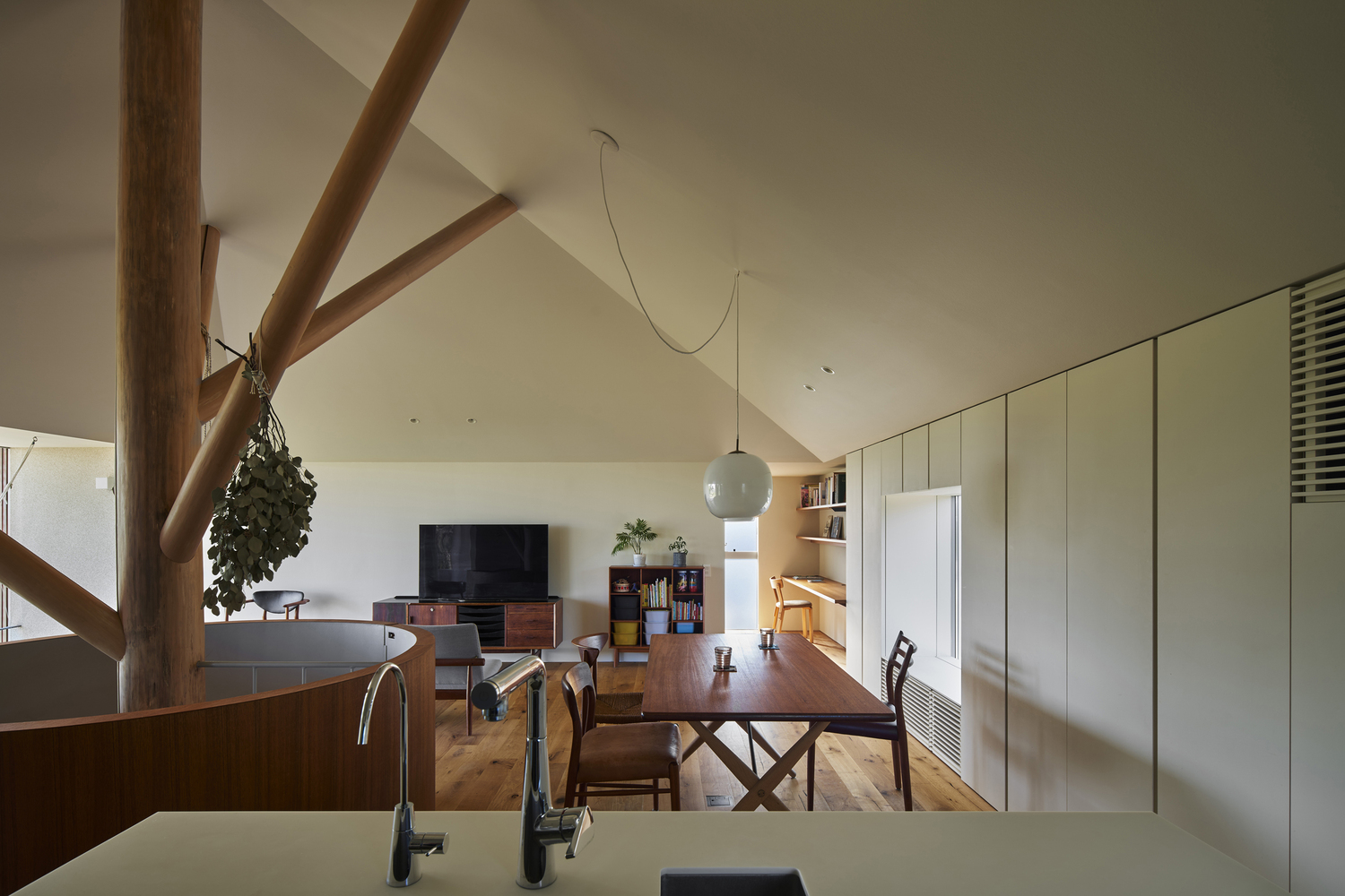 Open-plan living and dining space with exposed timber structure and vaulted ceiling under natural light