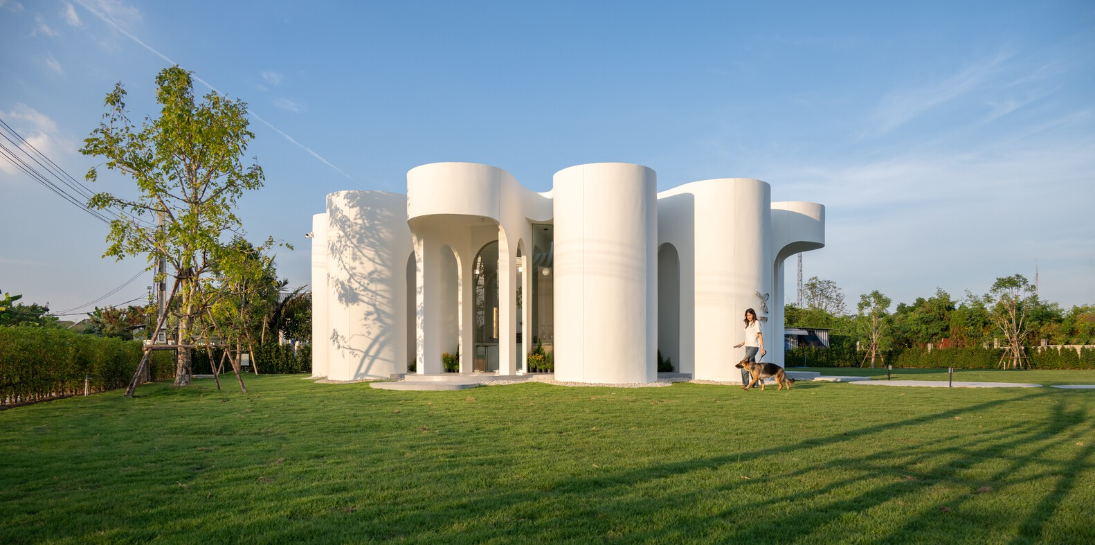 White cylindrical volumes grouped around a central void on a lawn in afternoon light
