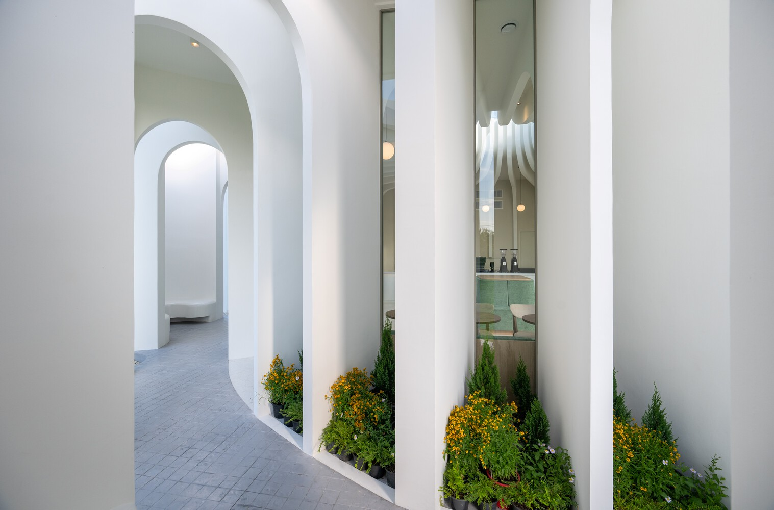 Curved corridor with planted beds of conifers between the white cylindrical columns