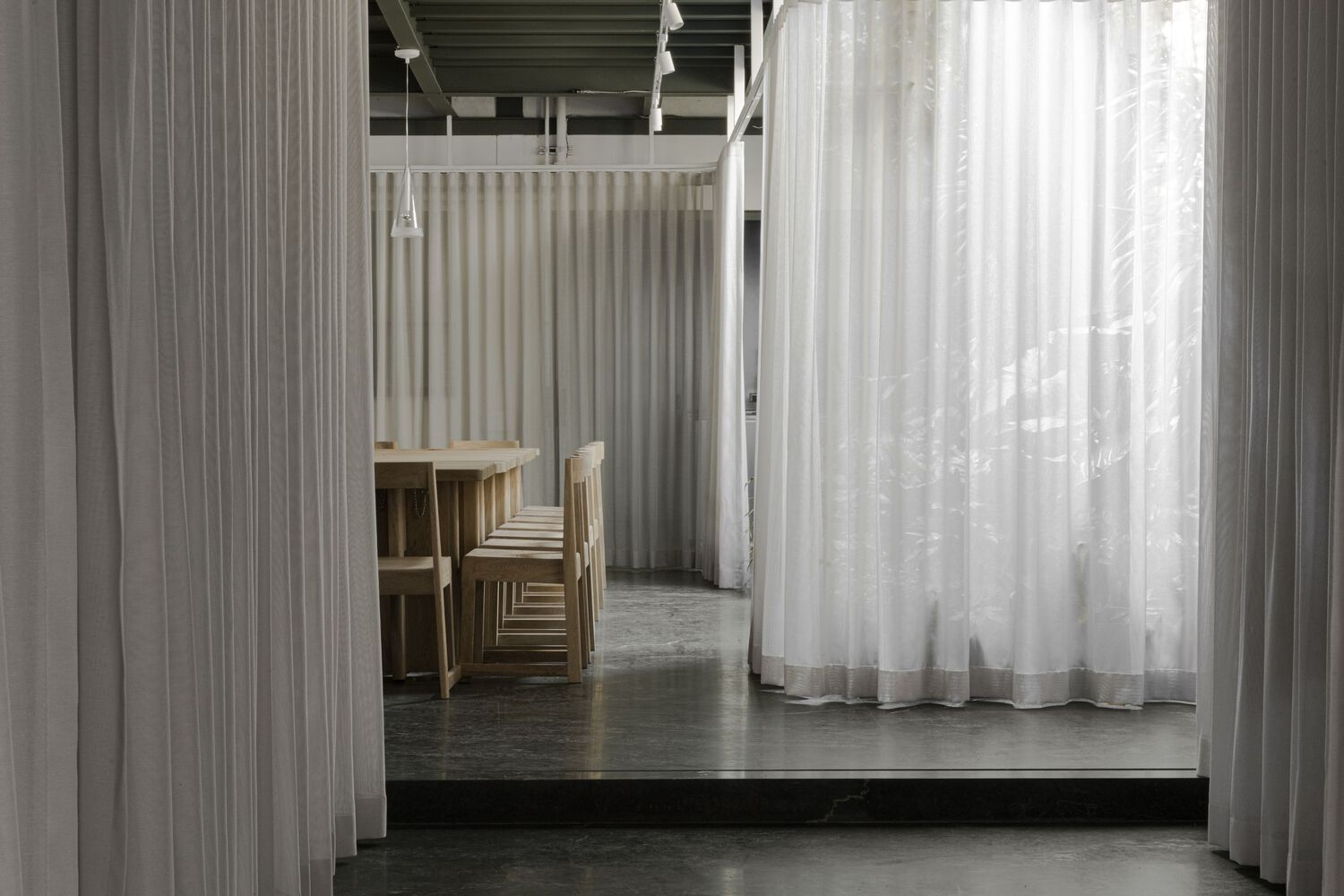 Corridor view through layered sheer curtains with timber furniture and exposed structural ceiling above
