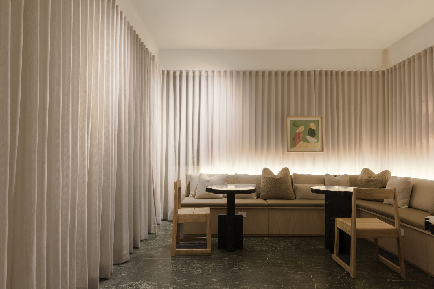 Seating alcove with timber benches and black side tables enclosed by floor-to-ceiling sheer curtains