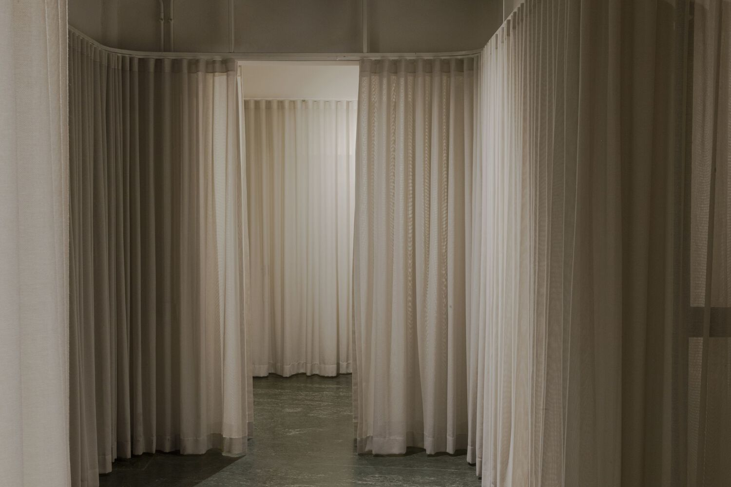 Corridor view framed by sheer white curtains hung from ceiling tracks on polished concrete floors