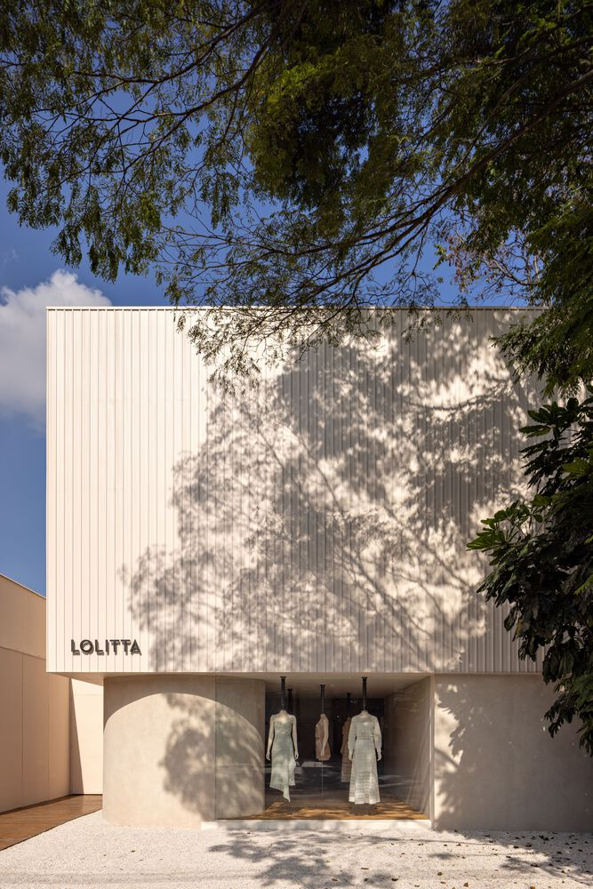 White corrugated metal facade with arched entry beneath dappled tree shadows