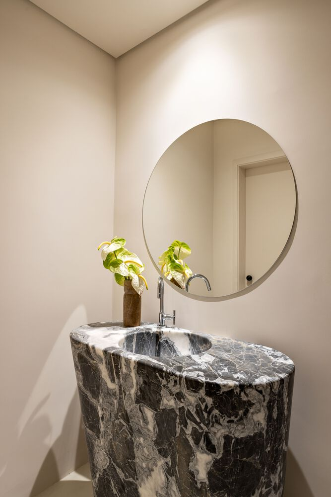 Cylindrical black and white marble vanity beneath a circular mirror in a powder room