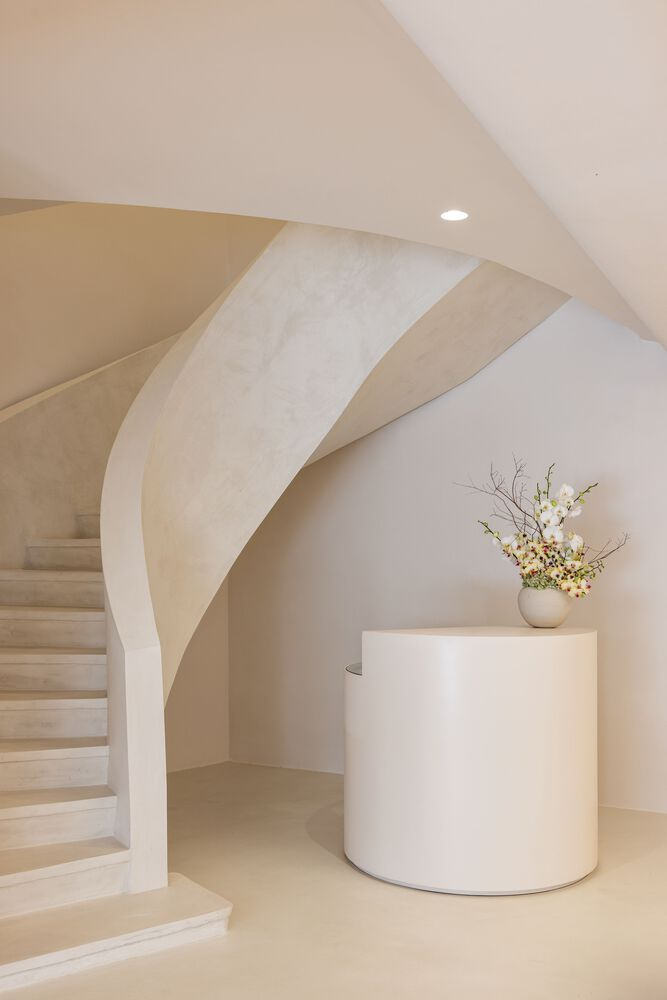Curved staircase with pale stone treads rising beside a cylindrical plinth holding a floral arrangement