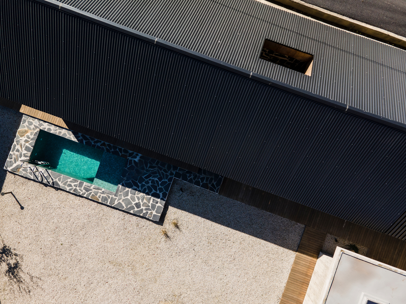 Overhead view of a courtyard pool with stone edging and corrugated metal cladding in bright sunlight