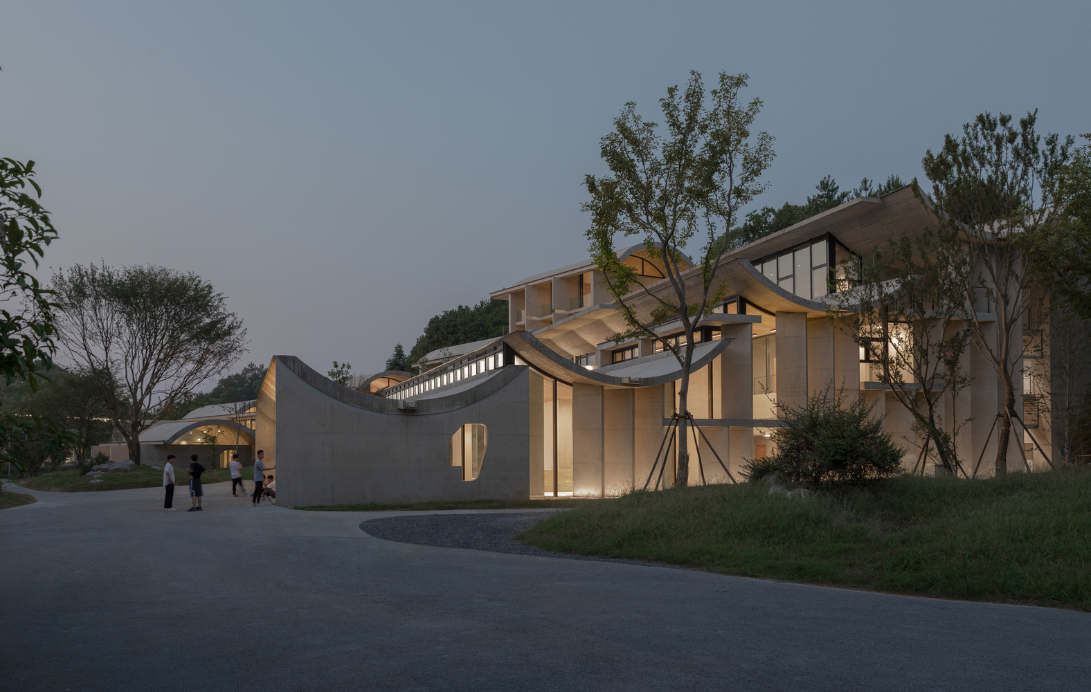 Cluster of vaulted concrete and glass pavilions illuminated at dusk with visitors gathering near the entrance
