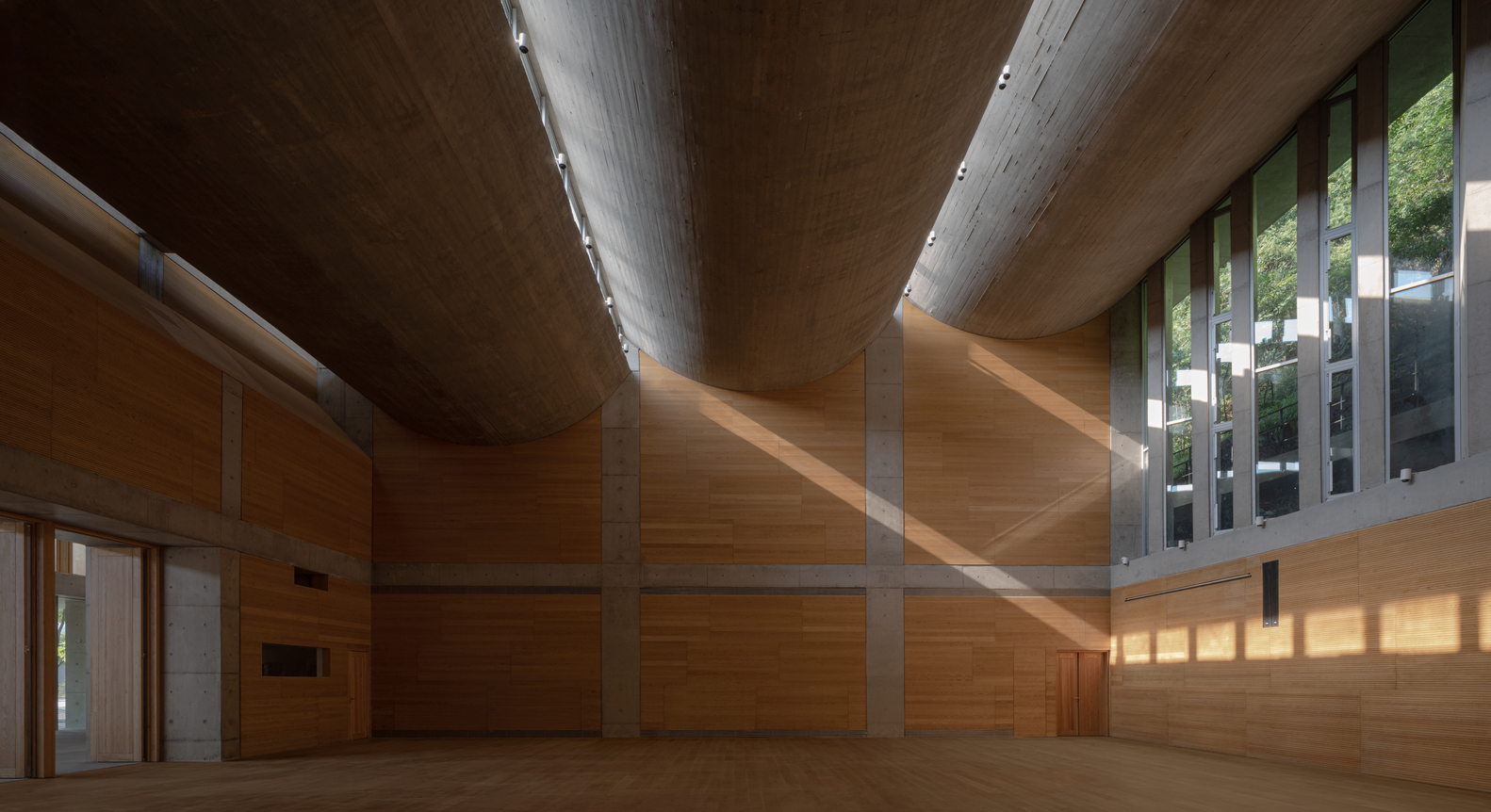 Interior courtyard with timber-clad walls and angular concrete ceiling planes pierced by clerestory windows above