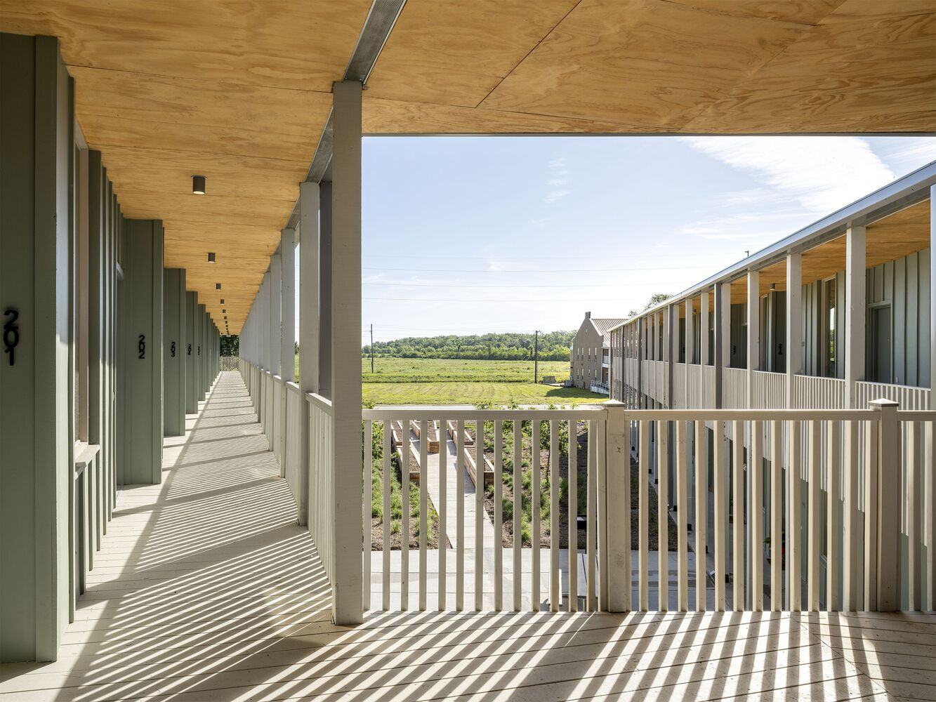 Upper-level walkway with white timber railings and plywood soffit casting striped shadows in afternoon light