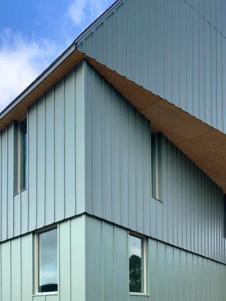 Close-up of layered gable roof edges where metal cladding meets plywood soffit beneath blue sky