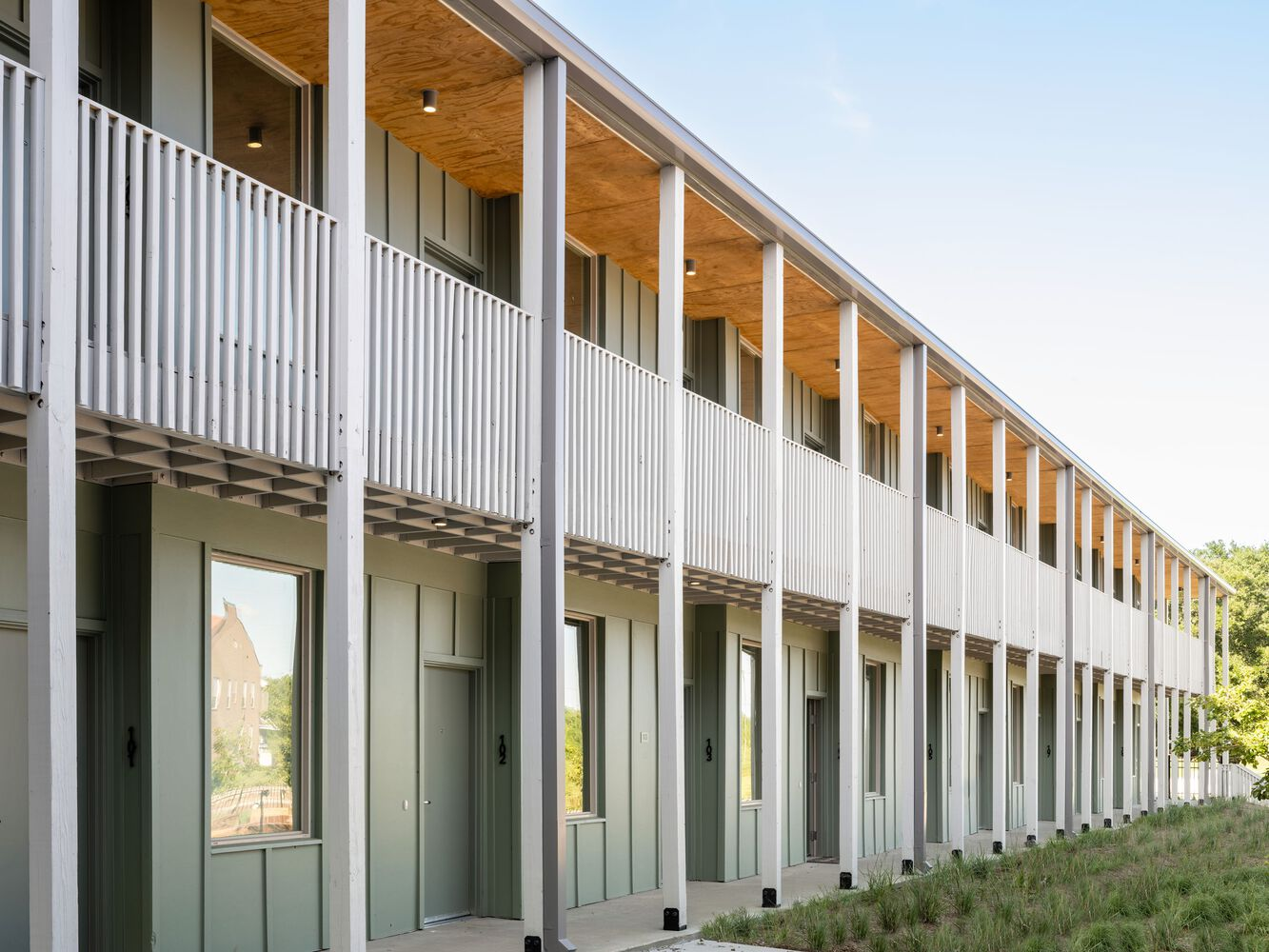 Two-story facade with metal cladding, white columns, plywood soffits, and upper-level balcony with vertical railings