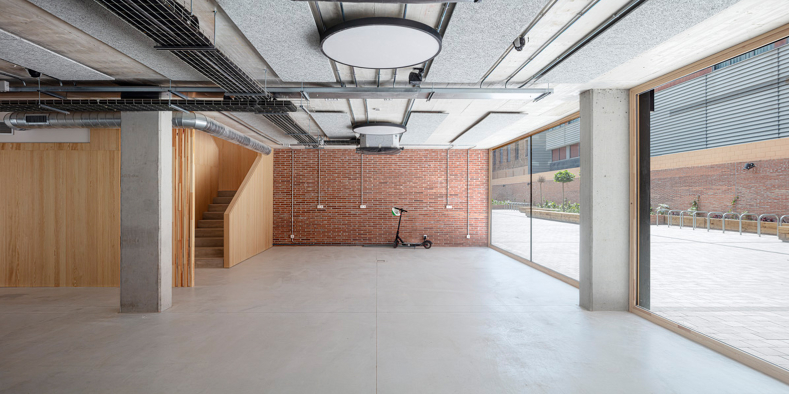 Interior space with exposed concrete columns, red brick wall and large glazed doors to courtyard