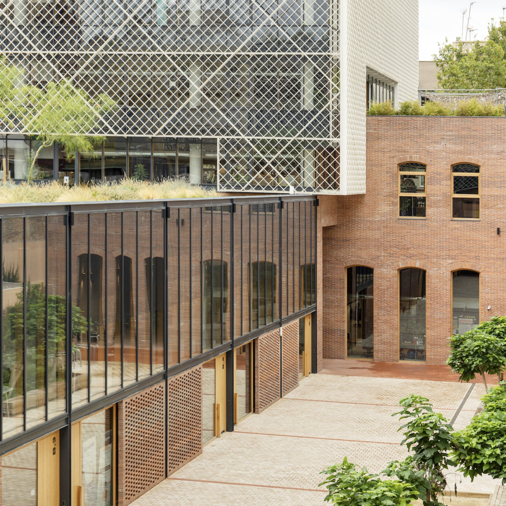 Courtyard view showing diagonal mesh facade cantilevering over retained brick facade with arched openings