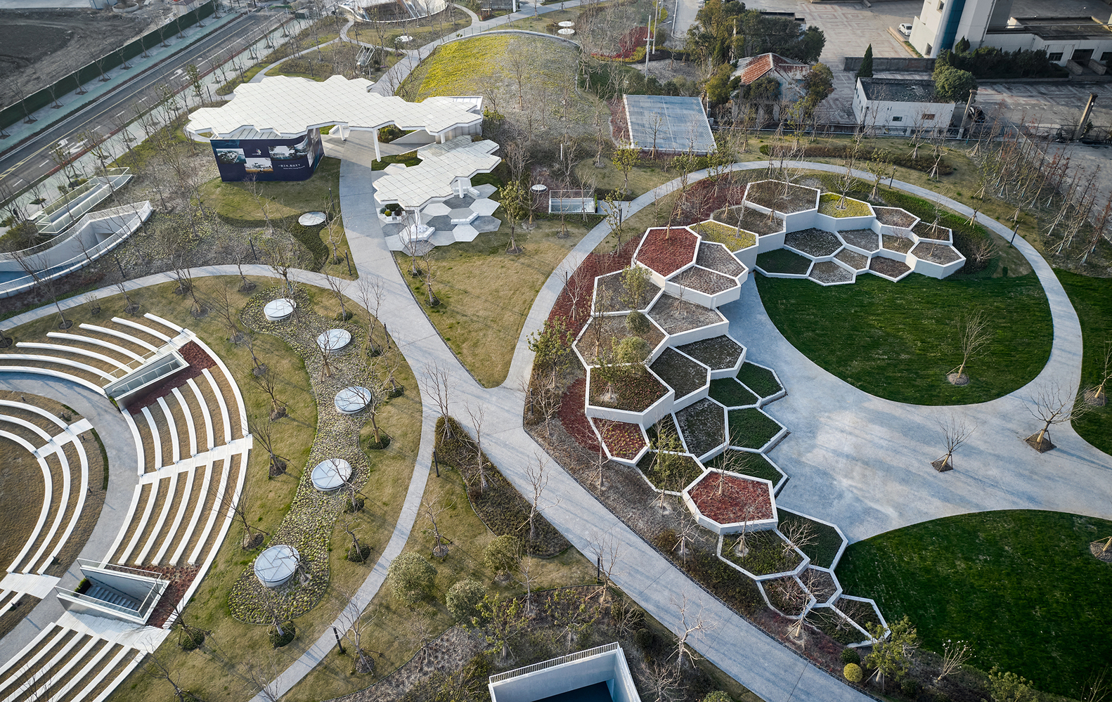 Aerial view of honeycomb-patterned planters and circular amphitheatre in a waterfront park with winter grass