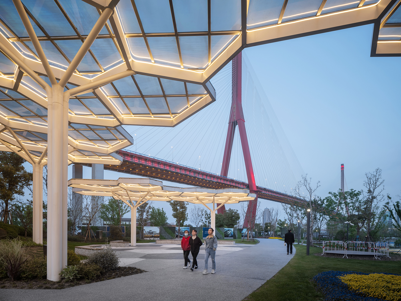 White steel pergola with hexagonal skylights framing view of red cable-stayed bridge at dusk