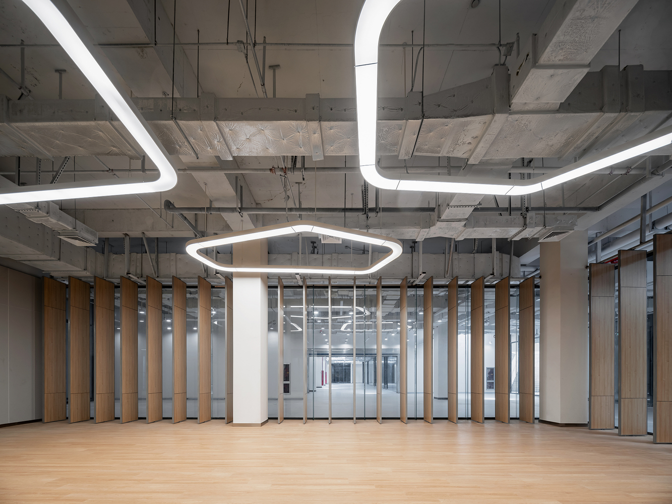Interior hall with exposed concrete ceiling, suspended hexagonal light fixtures, and vertical timber screen partition