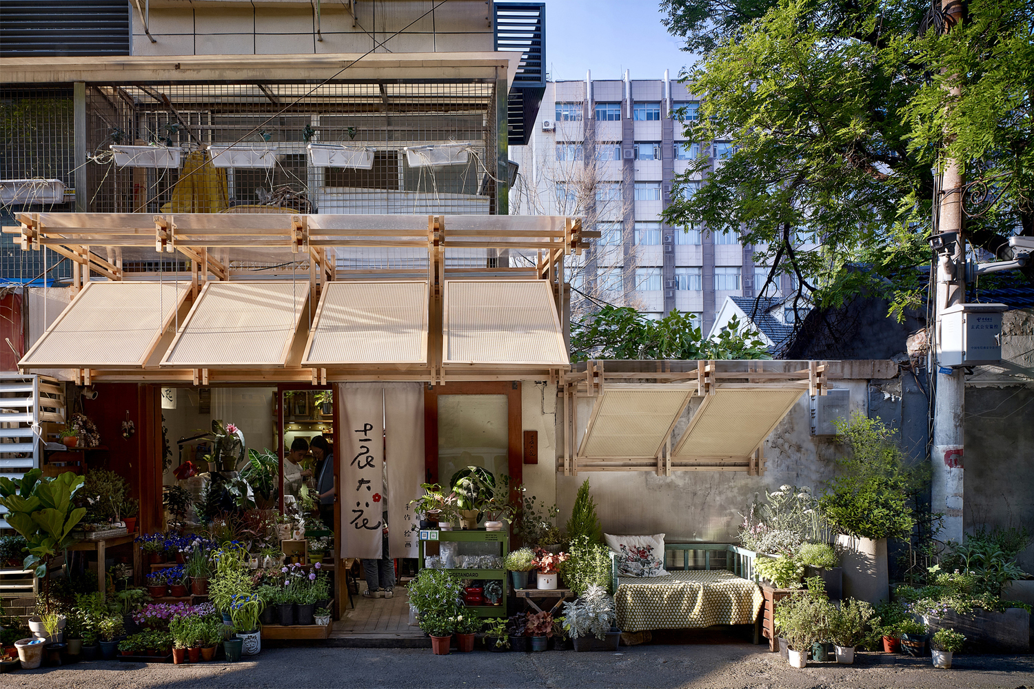 Street view of the timber-framed canopy structure with fabric awnings sheltering a flower shop and potted plants