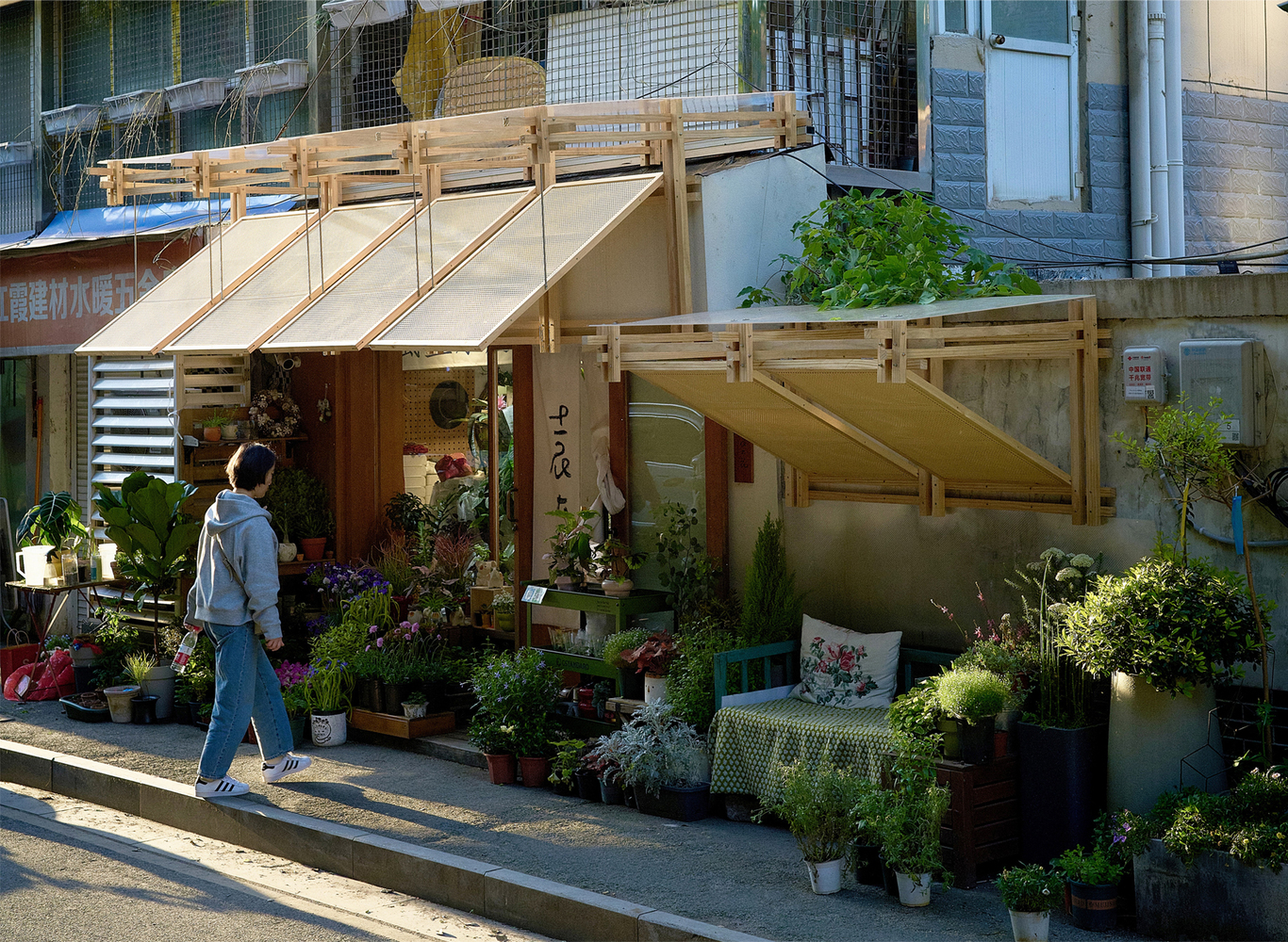 Pedestrian passing the storefront with its angled timber canopy and display of potted plants in morning light