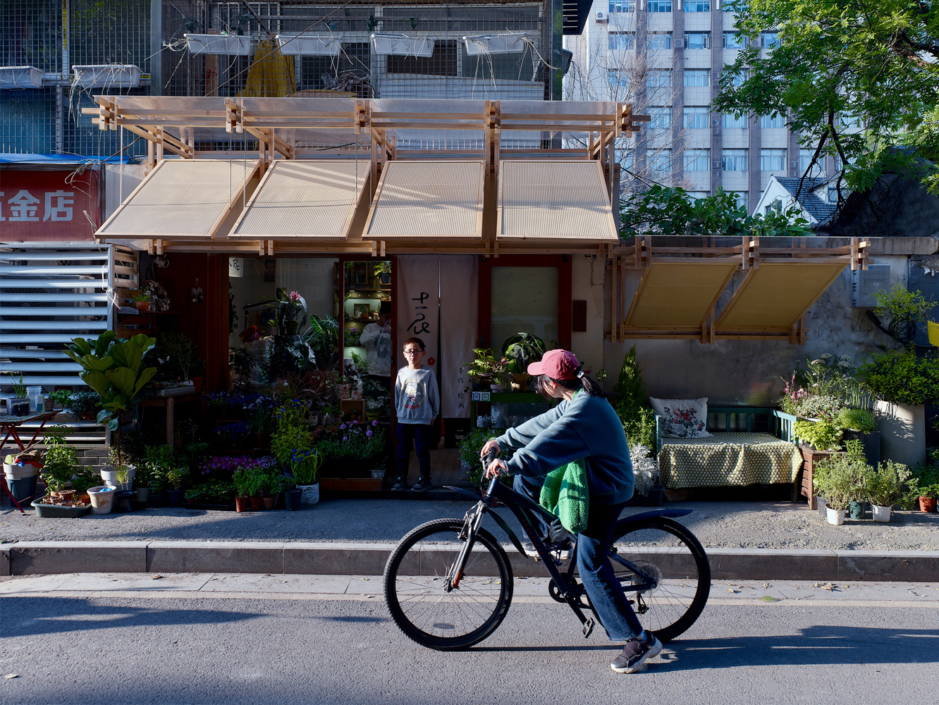 Facade with adjustable timber awnings as a cyclist passes in afternoon light