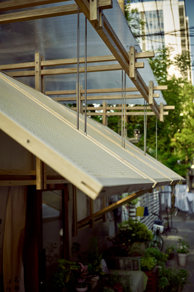 Detail of the hinged timber awning with perforated metal panel and cable supports at dusk