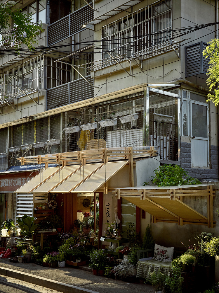 Shopfront with pivoting timber awnings inserted below the existing residential building with metal railings