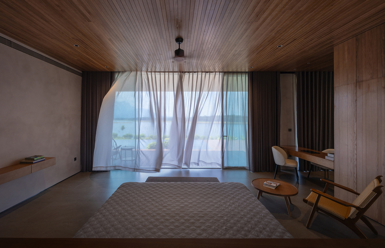 Bedroom with timber-paneled ceiling and sheer curtains billowing over floor-to-ceiling glass doors
