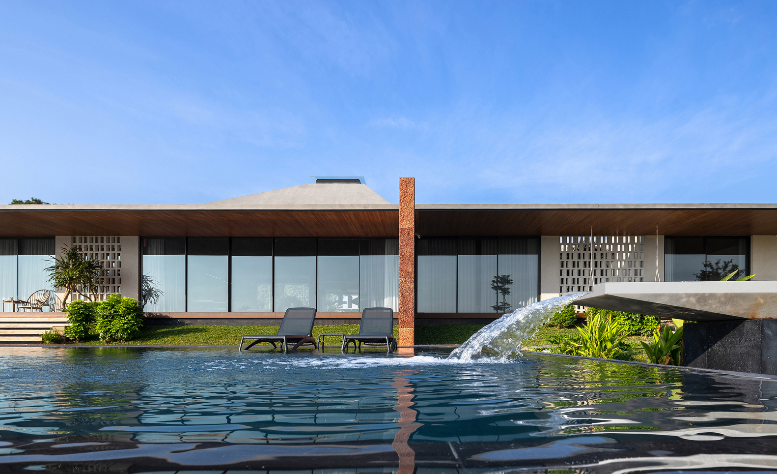 Rear facade with continuous glazing and overhanging roof reflected in the pool under midday sun