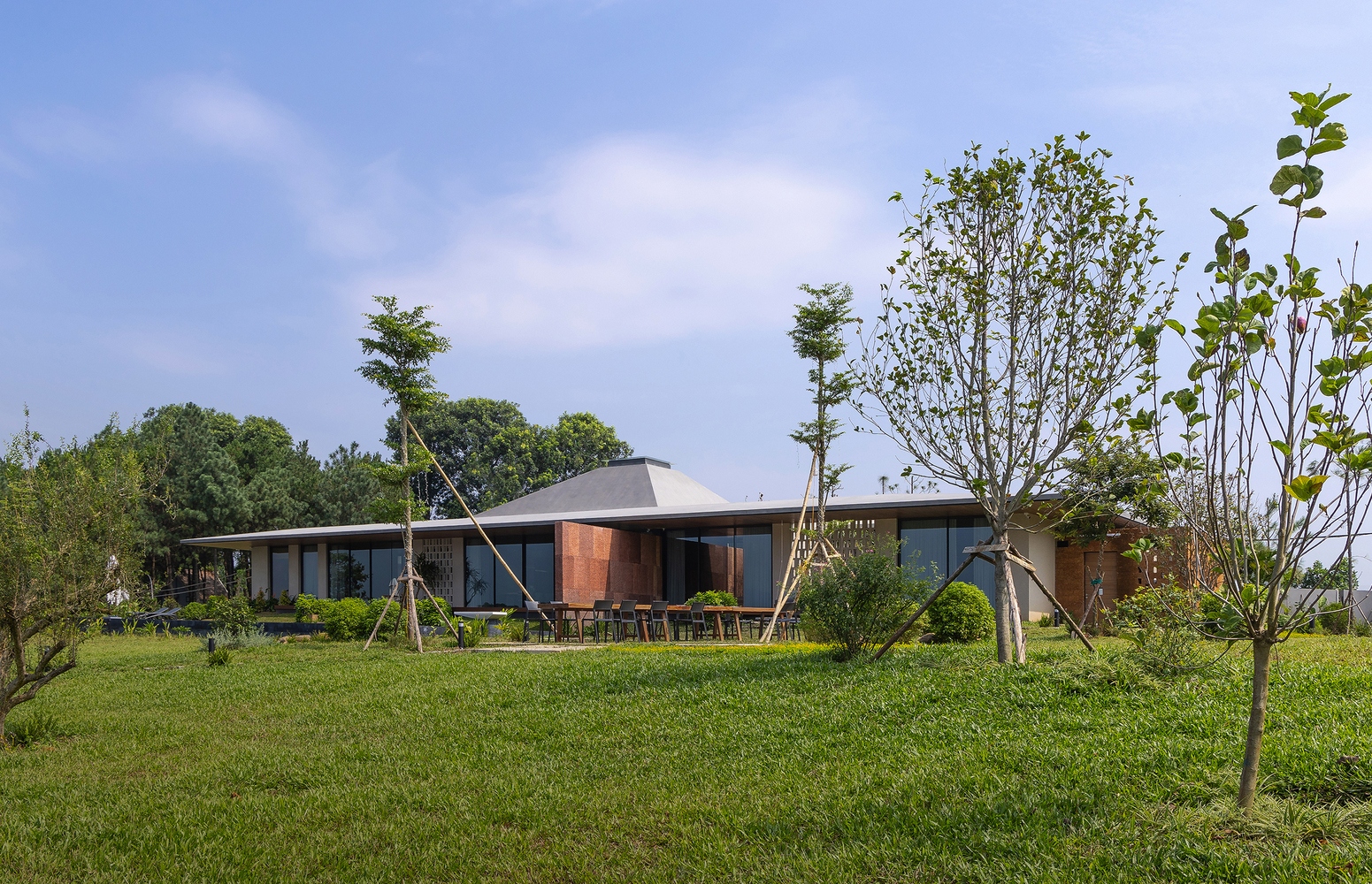 Low horizontal volume with overhanging roof set in a grassy clearing with young trees scattered around it