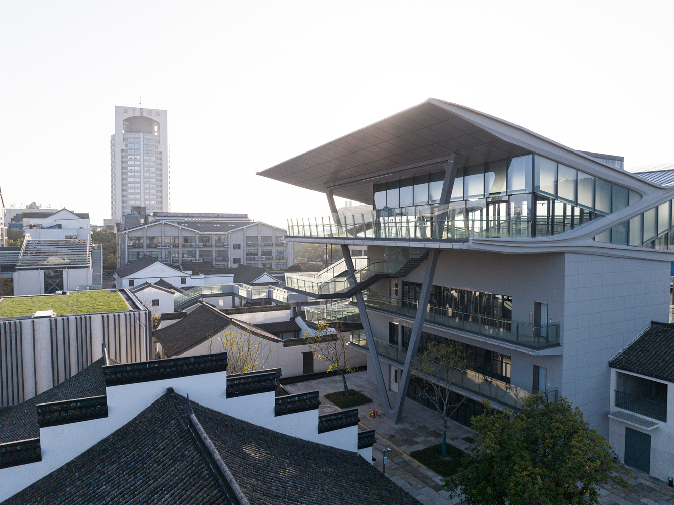Elevated view of the glazed upper volume with its angular cantilevered roof among courtyard buildings and rooftops
