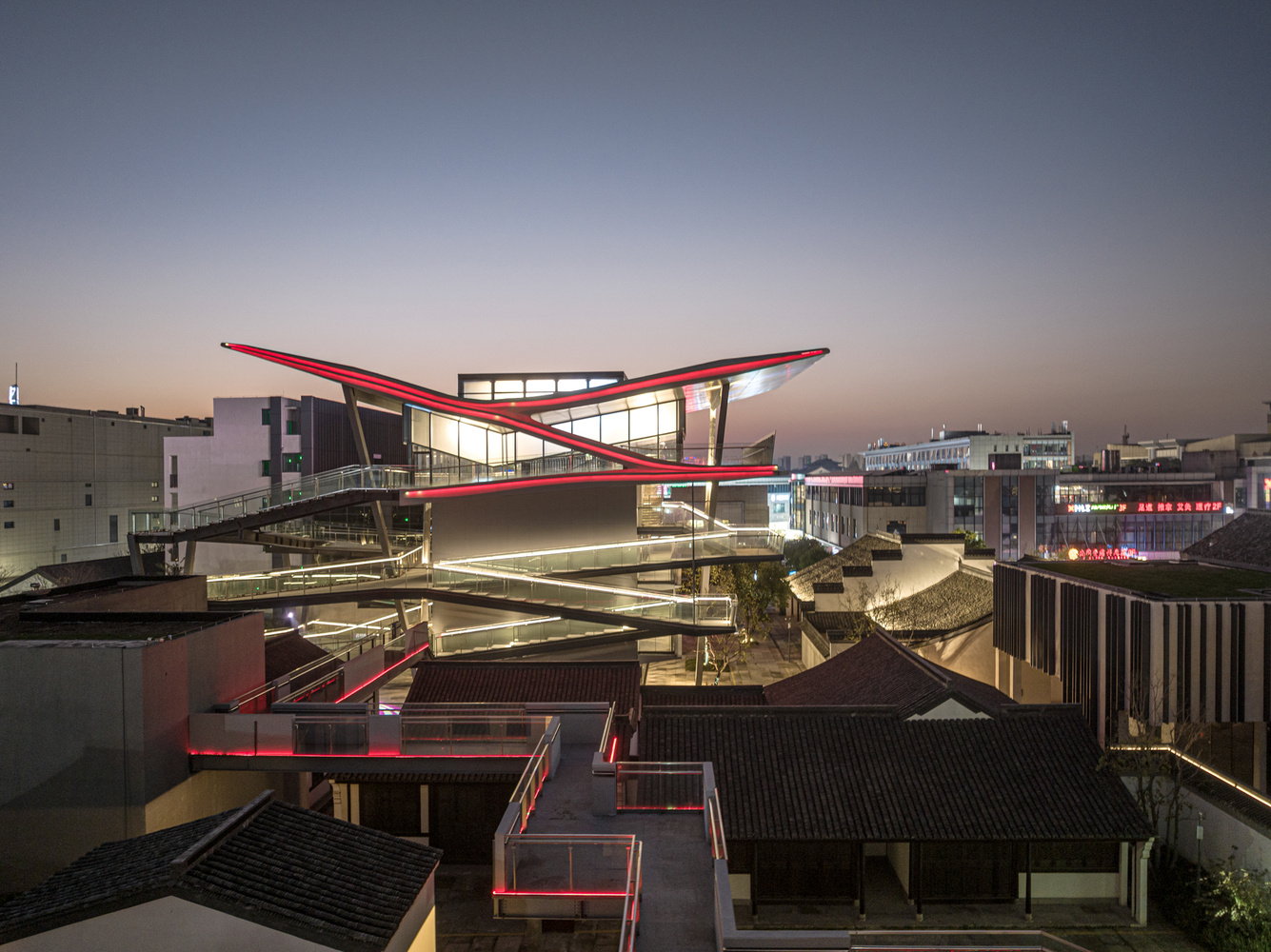 Night view of the illuminated winged roof rising above preserved traditional tile-roofed structures and pathways