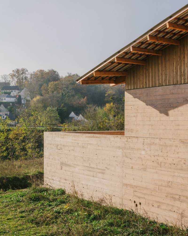 Rammed earth retaining wall and exposed timber roof structure with autumn foliage in the background