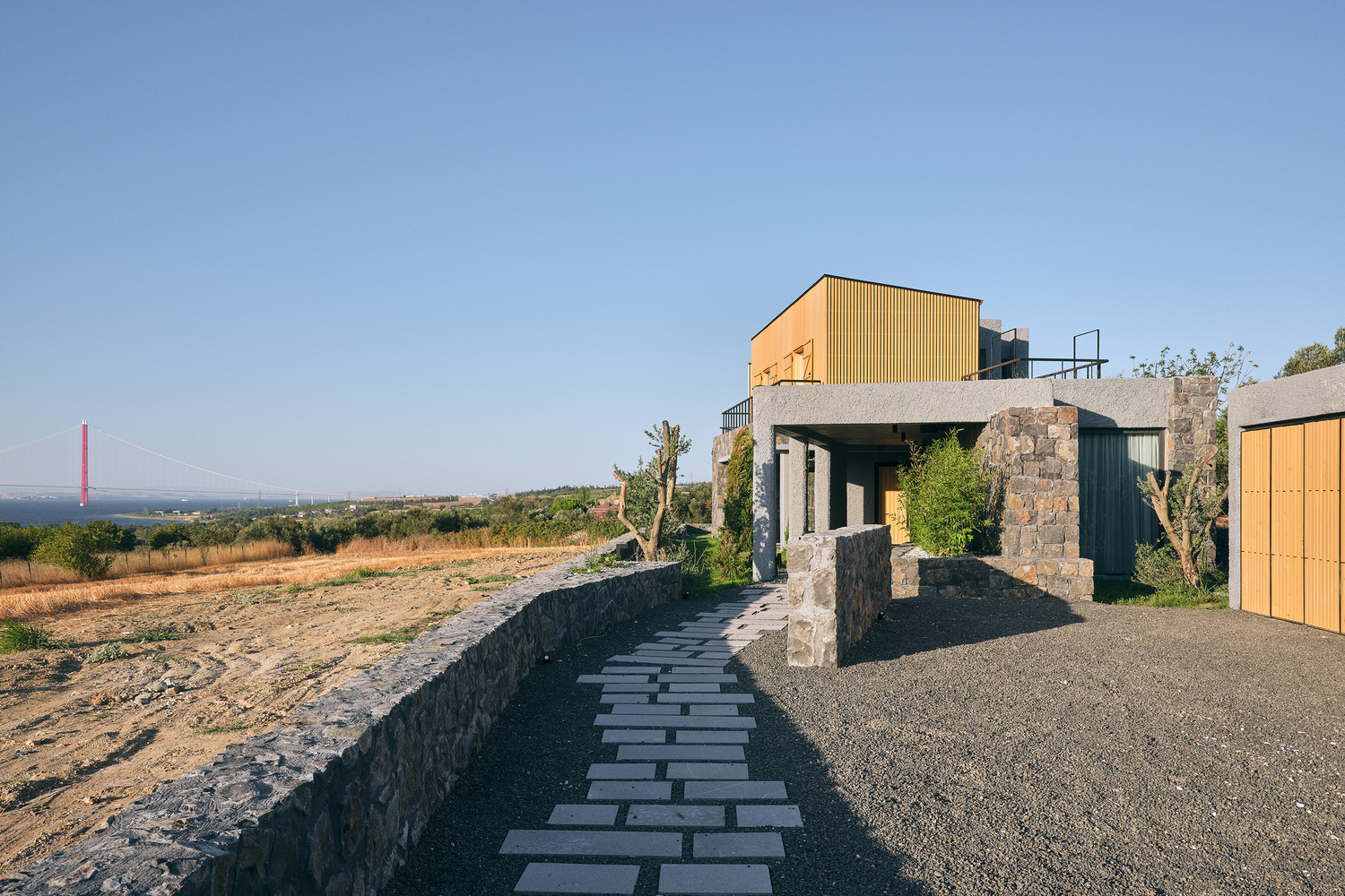 Stone paved entry path leading to the stone and timber volume set among vineyards at dusk