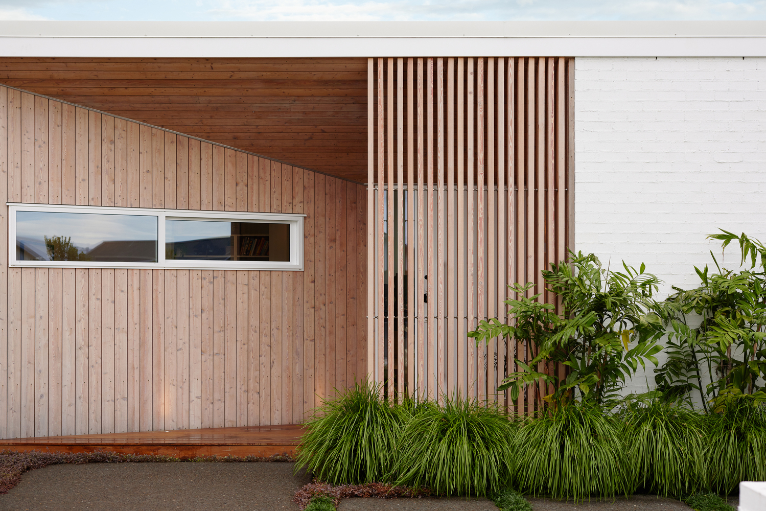 Timber-clad facade with vertical slat screen and horizontal ribbon window beside planted garden bed