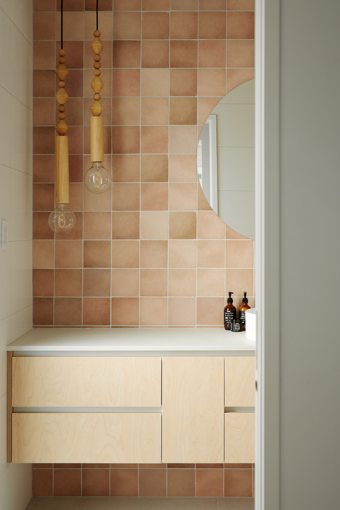 Bathroom vanity with pale plywood cabinetry beneath gradient terracotta tile wall and timber pendant lights