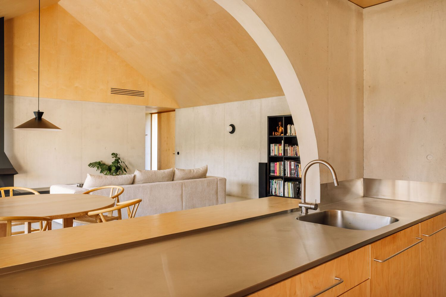 Open kitchen with timber cabinetry and stainless steel countertop beneath arched plywood ceiling with recessed vent grille