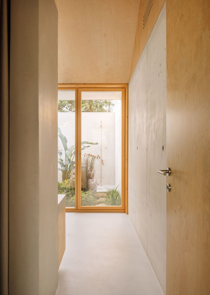 Narrow corridor with plywood doors and ceiling leading to a timber-framed window overlooking a courtyard