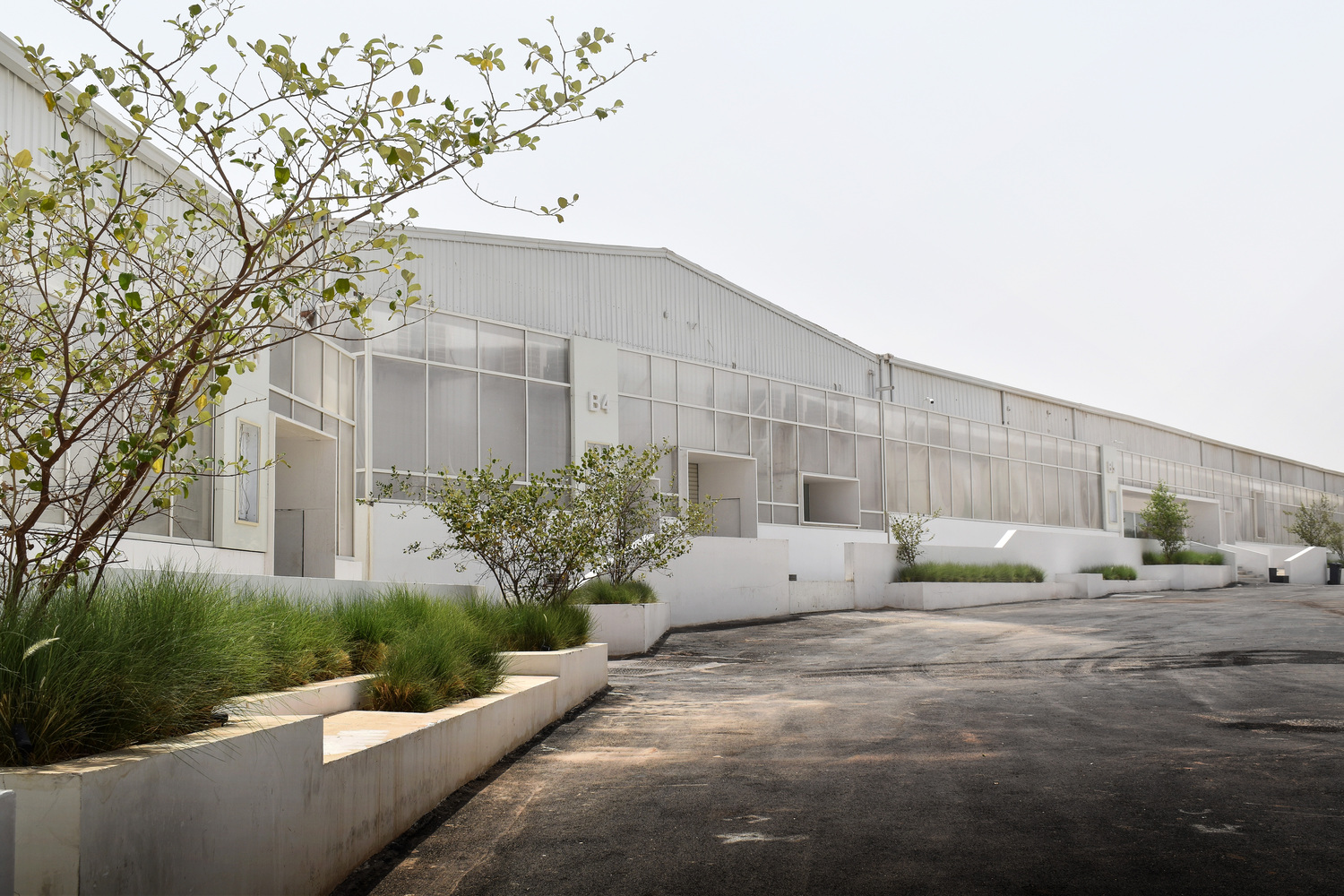 Long facade with translucent panels and concrete planters with grasses along a worn asphalt road